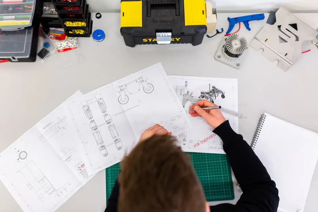 Person reviewing technical blueprints at a workbench with tools