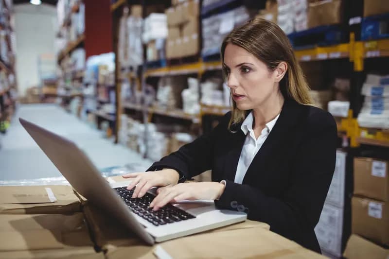 Analyst reviewing records on a laptop in a warehouse aisle