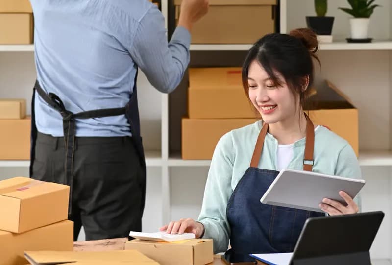 Two small-business sellers packing and checking parcels in a stockroom